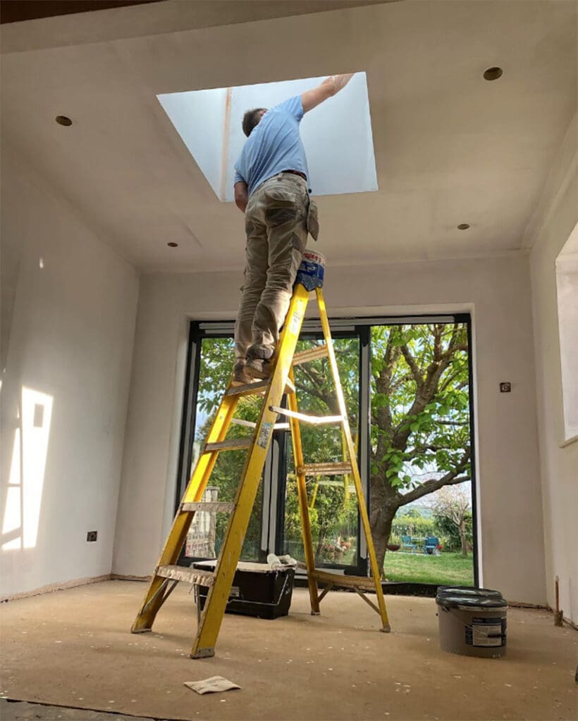 workman in pale blue shirt standing on ladder, to refurbishing home
